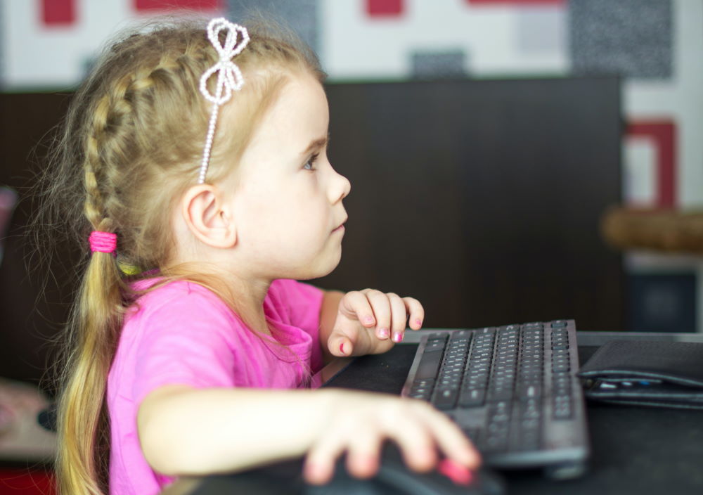 A young girl using a computer and mouse.